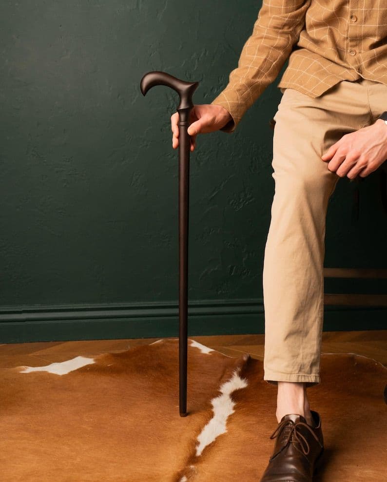 A man seated at home, resting his hand on a dark derby cane